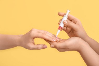 Sarı arka planda kalemle tırnak altı yağı süren kadın eller, yakın plan.