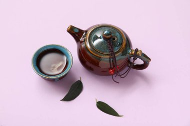 Çin çaydanlığı, bir fincan sıcak çay ve mor arka planda yapraklar.