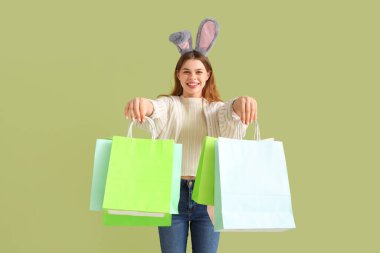 Yeşil arka planda alışveriş torbaları olan tavşan kulaklı genç bir kadın. Paskalya kutlaması
