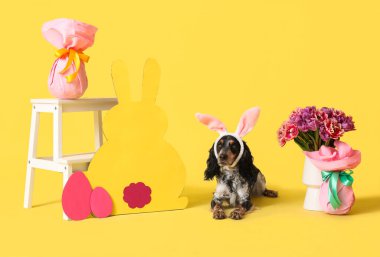 Güzel laleleri, Paskalya hediyesi yumurtaları ve sarı arka planda kağıttan tavşanı olan tavşan kulaklı şirin cocker spaniel.