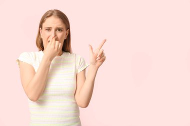 Young woman feeling disgusting smell and pointing at something on pink background clipart