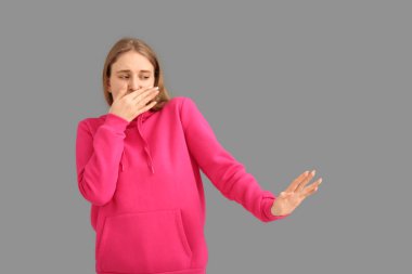 Gri arka planda korkunç bir koku hisseden genç kadın.