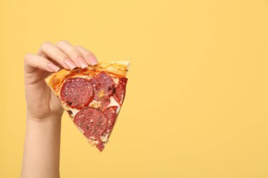 Sarı arka planda lezzetli bir pizza dilimi tutan kadın.