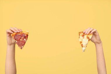 Sarı arka planda lezzetli pizza dilimleri tutan kadın eller.