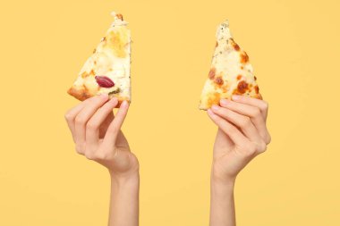 Sarı arka planda lezzetli pizza dilimleri tutan kadın eller.