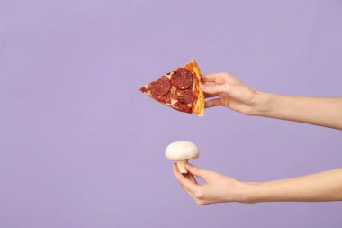 Leylak arka planında pizza dilimi ve mantar tutan kadın eller.