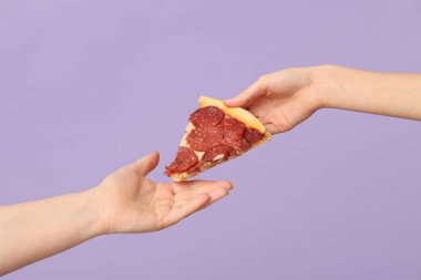 Kadın eli, leylak arkaplanda lezzetli bir pizza dilimi veriyor.