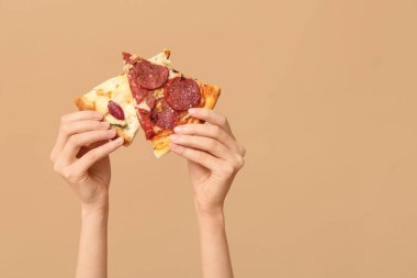 Kadın elleri bej arka planda lezzetli pizza dilimleri tutuyor.