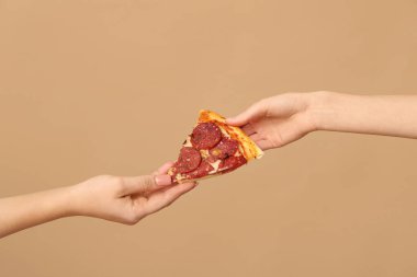 Kadın eli bej arka planda lezzetli bir pizza dilimi veriyor.