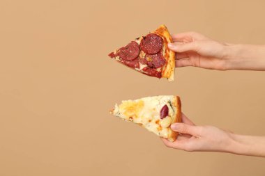 Kadın elleri bej arka planda lezzetli pizza dilimleri tutuyor.