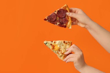 Turuncu arka planda lezzetli pizza dilimleri tutan kadın eller.