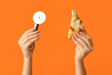 Lezzetli pizza dilimleri ve turuncu arka planda pizza kesicisi tutan kadın eller.