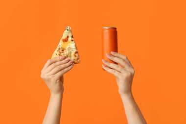 Kadın eli, lezzetli pizza dilimleri ve turuncu arka planda bir kutu gazoz tutuyor.