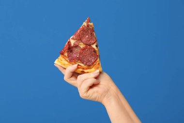 Mavi arka planda lezzetli bir pizza dilimi tutan kadın.