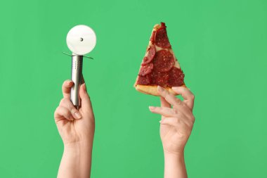 Lezzetli pizza dilimleri ve yeşil arka planda pizza kesicisi tutan kadın eller.
