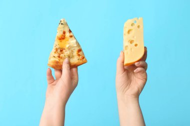 Kadın elleri mavi arka planda lezzetli pizza dilimleri ve peynirler tutuyor.