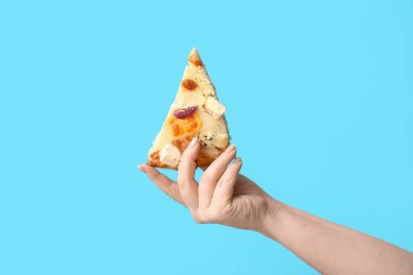 Mavi arka planda lezzetli bir pizza dilimi tutan kadın.