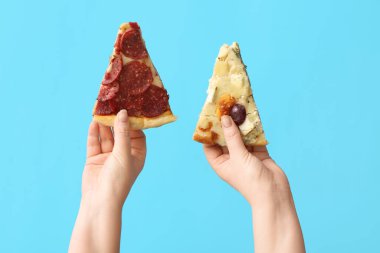 Mavi arka planda lezzetli pizza dilimleri tutan kadın eller.