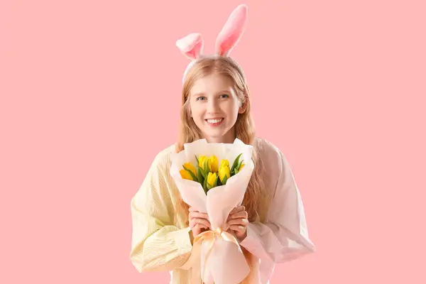 ピンクの背景にイースターバニーの耳と花を持つ若い女の子 — ストック写真
