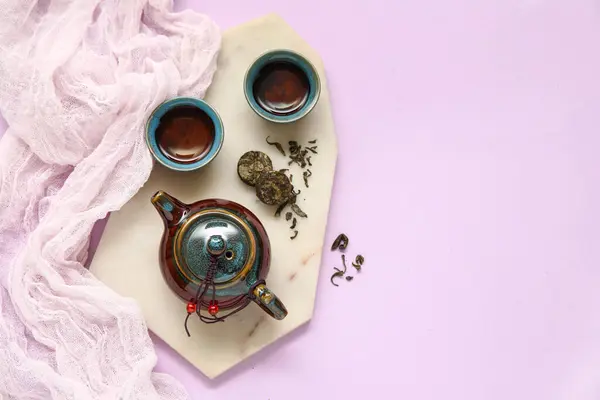 stock image Marble tray with teapot, cups of tea and dry pressed tea on purple background