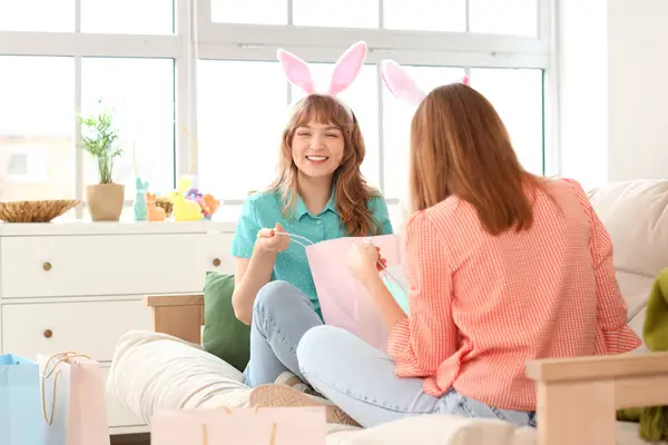 Happy young women in bunny ears headbands unpacking shopping bags for Easter at home