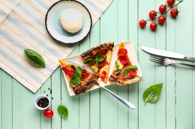 Lezzetli pizza dilimli Margarita, taze domates ve yeşil ahşap arka planda Mozzarella peyniri.