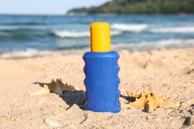 Bir şişe güneş kremi ve kumsalda okyanus kenarında deniz yıldızları.