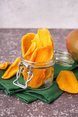 Jar with slices of dried mango on dark table clipart