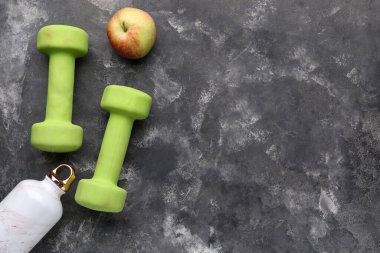 Dambıllar, su şişesi ve siyah arka planda elma.