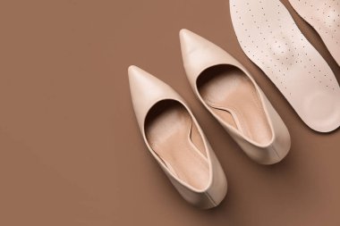 Bir çift ortopedik taban ve arka planda yüksek topuklu ayakkabı.