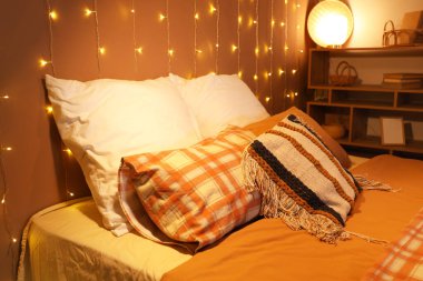 Geceleri yatak odasında yumuşak yastıklı ve parlayan ışıklar olan büyük bir yatak.