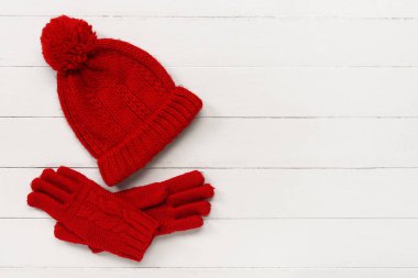 Beyaz ahşap arka planda sıcak şapkalı kırmızı örgü eldivenler.