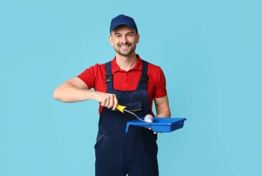Mavi arka planda boya silindirli ve tepsisi olan erkek ressamın portresi
