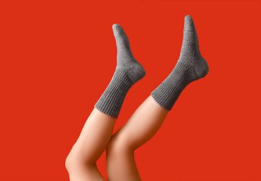 Kırmızı arka planda, sıcak gri örgü çoraplı genç kadın bacakları.