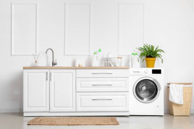 Lavabosu, çamaşır makinesi ve çamaşır sepetiyle aydınlatma odasının içinde.