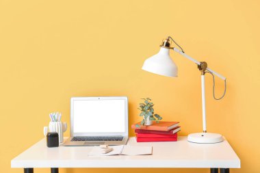 Laptop, lamba ve renkli duvarın yanındaki masada rahat bir ofis.