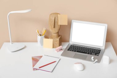 Ofisteki masada dizüstü bilgisayar, kablosuz kulaklık, lamba ve defter.