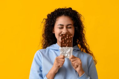 Sarı arka planda çikolata çubuğu olan güzel bir Afro-Amerikalı kadın.