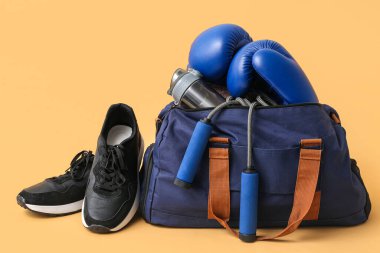 Spor giyimli spor çantası ve bej arka planda boks eldivenleri.