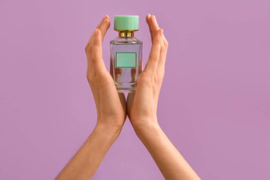 Kadın eli, arka planda parfüm şişesini tutuyor.