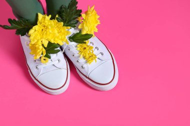 Pembe arka planda sarı kasımpatı çiçekleri olan beyaz ayakkabılı güzel genç kadın bacakları.