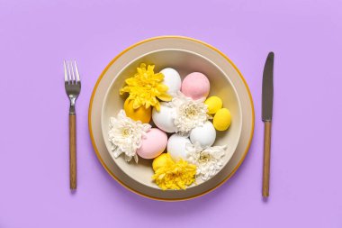 Paskalya yumurtaları ve eflatun arkaplanda kasımpatı çiçekleri olan güzel bir masa.