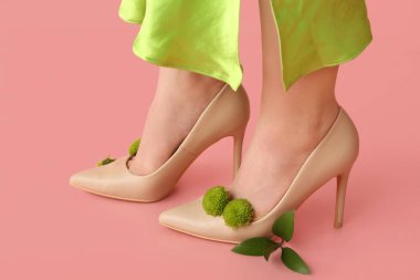Pembe arka planda kasımpatı çiçekleri olan yüksek topuklu güzel genç bayanların bacakları.