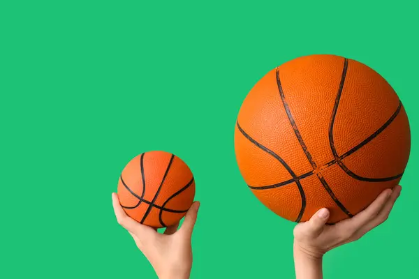 Female hands with balls for playing basketball and kettlebell on green background