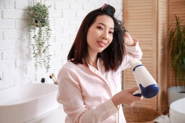 Güzel Asyalı bir kadın banyoda saçlarını kurutuyor.