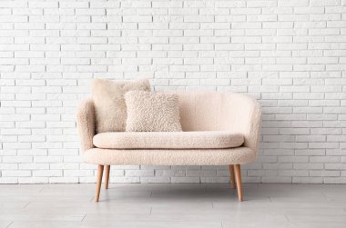 Tuğla duvarın yanında yastıkları olan rahat beyaz bir kanepe.