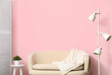 Sıcak beyaz kanepe, battaniye ve lamba pembe duvarın yanında.