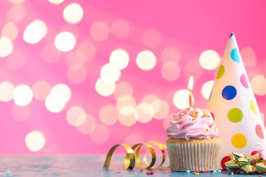 Bulanık ışıklara karşı yanan mum ve parti şapkası olan leziz bir doğum günü keki.