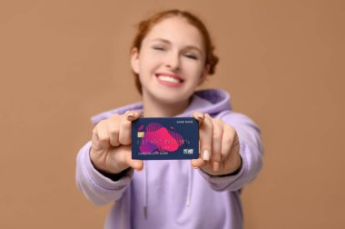 Kahverengi arka planda kredi kartı olan güzel bir genç kadın.