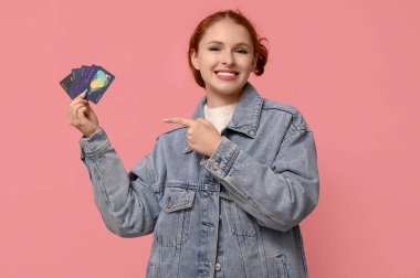 Pembe arka planda kredi kartlarını gösteren güzel genç bir kadın.